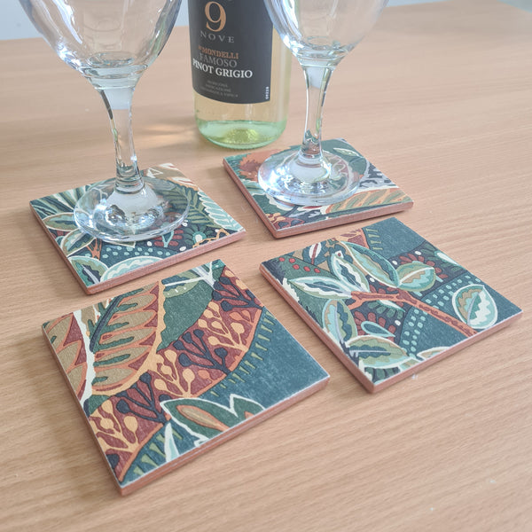 Handmade Nature's Exhibitionists pattern ceramic coaster showing dramatic botanical floral design on coffee table with wine bottle and glasses