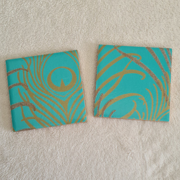 Pair of teal ceramic coasters with a gold peacock feather pattern and added glitter.