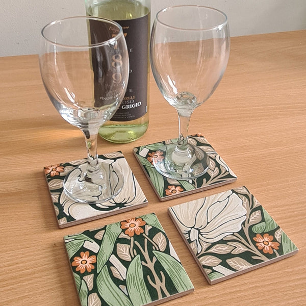 William Morris Pimpernel handmade coaster set displaying Art Nouveau floral design in green, cream and orange colours, with wine bottle and glasses