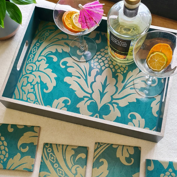 A teal and champagne damask baroque-inspired serving tray with matching coasters, styled with two coupe glasses, orange slices, and a bottle on a light tabletop.