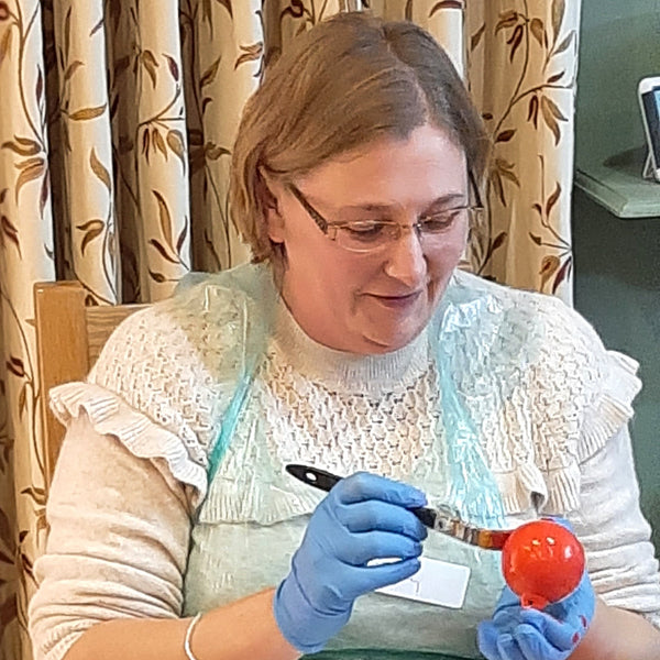 A festive party goer painting her ceramic baubles in Christmas red at a Baubles and Bubbles party.