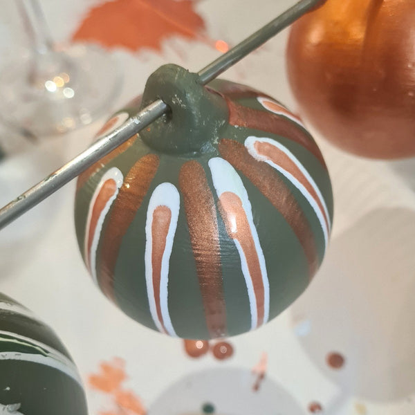 Hand-painted ceramic bauble, decorated with a dark green base, metallic copper-drizzles, and white painted accents.