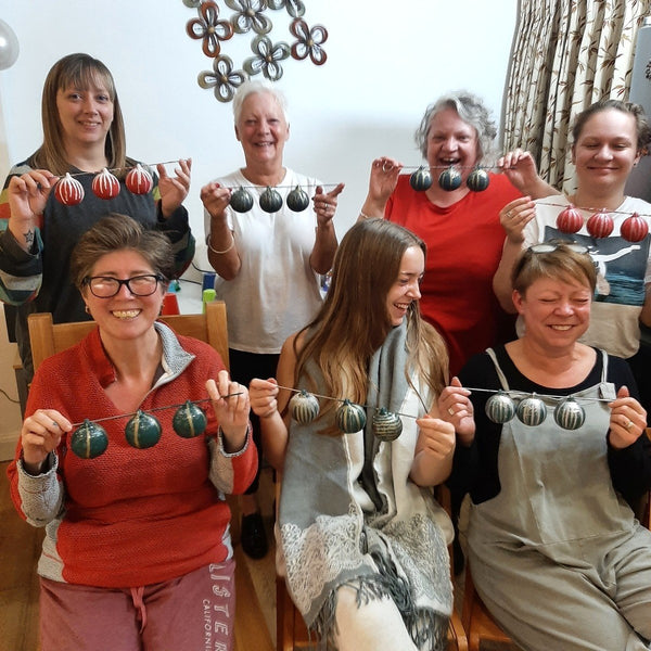 A family of seven women smiling and holding up their painted baubles at a Baubles & Bubbles party in Stotfold.