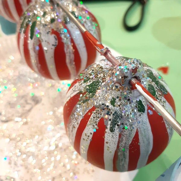 A close-up of a decorative Christmas bauble with red base, white candy cane drizzles, covered in silver glitter, created at a Baubles & Bubbles Christmas party in Stotfold.