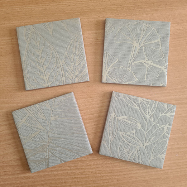 Limited-edition set of four handmade ceramic coasters with sage green ginkgo leaves and metallic Champagne details.