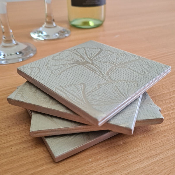 Close-up of metallic Champagne ginkgo leaves on a soft sage green handmade ceramic coaster.