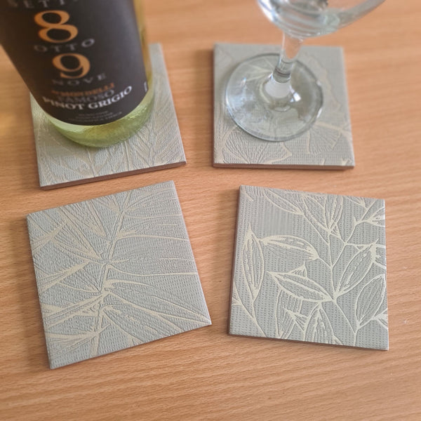 Handmade sage green ceramic coasters featuring delicate ginkgo leaves with metallic Champagne highlights.