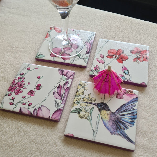 Set of four handmade Hummingbird Floral ceramic coasters on coffee table with cocktail umbrella.