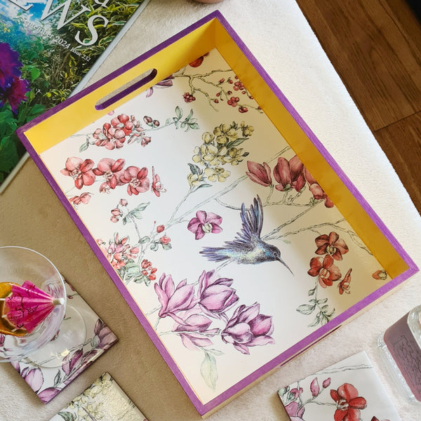 Angled view of handcrafted hummingbird floral serving tray with deep yellow painted sides and metallic violet edging.
