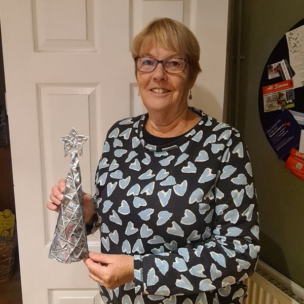 Handmade silver embossed aluminium Christmas tree decoration with star topper, creation proudly shown by a beginner.