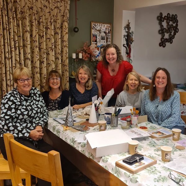 Six women smiling together around a craft table filled with supplies and embossing kit creations at a craft class in Stotfold.