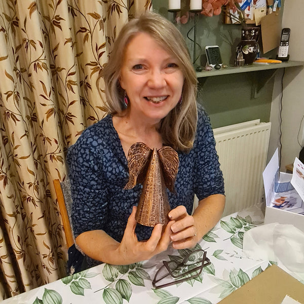 A smiling woman with blonde hair holds a decorative copper angel she has created at a metal embossing craft class in Stotfold.