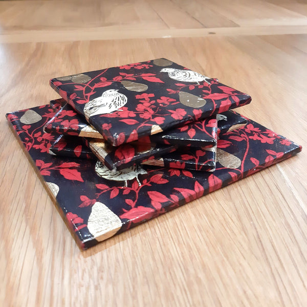 One-of-a-kind Partridge in a Pear Tree set with four ceramic coasters and matching bottle stand, stacked on a coffee table.