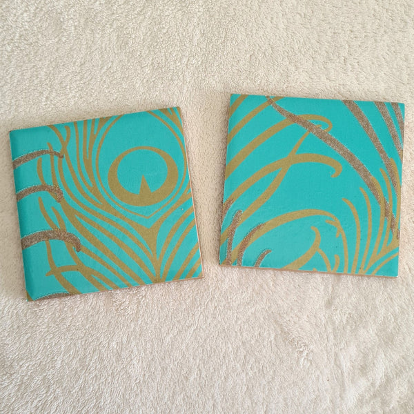 shimmering teal peacock feather design on a handmade ceramic coaster pair.