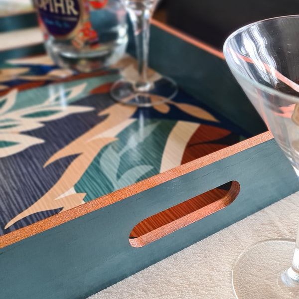 Deep teal handcrafted wooden serving tray with integrated handles and metallic copper edging.