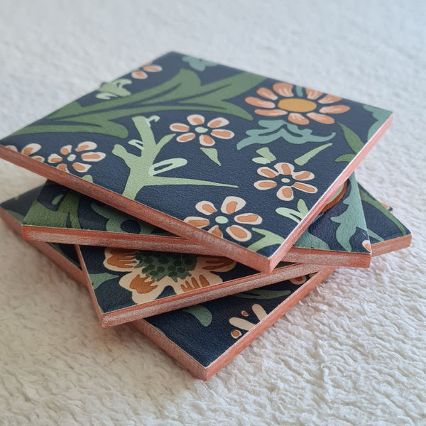 Handmade Blackthorn ceramic coasters in Slate Blue, stacked in a set of 4 showing flowers, leaves and twisting botanical forms with copper metallic edging.