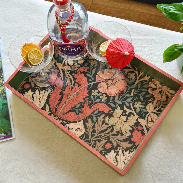 Handcrafted William Morris Compton wooden serving tray in autumnal colours with deep sage green paint and rusty red metallic edging, styled on a coffee table with cocktail glasses and bottle.
