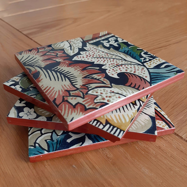 Stacked William Morris Wandle ceramic coasters showing their handcrafted rusty red metallic edging.