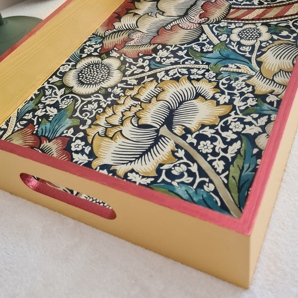 Angled view of Mustard yellow William Morris Wandle wooden serving tray with integrated handles and rusty red metallic edging.