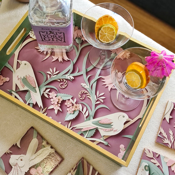Handcrafted sage green wooden serving tray decorated with woodland animals and foliage on a rich plum background with metallic gold edging. Styled with cocktail glasses and a bottle.