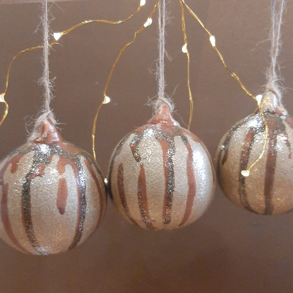 Set of 3 uniquely painted Christmas baubles in gold, brown and glitter, strung with natural twine, hanging in lights